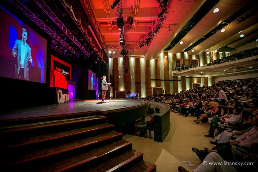 Mykola Latansky speaking on the TEDx Chennai stage, with the auditorium visible alongside it